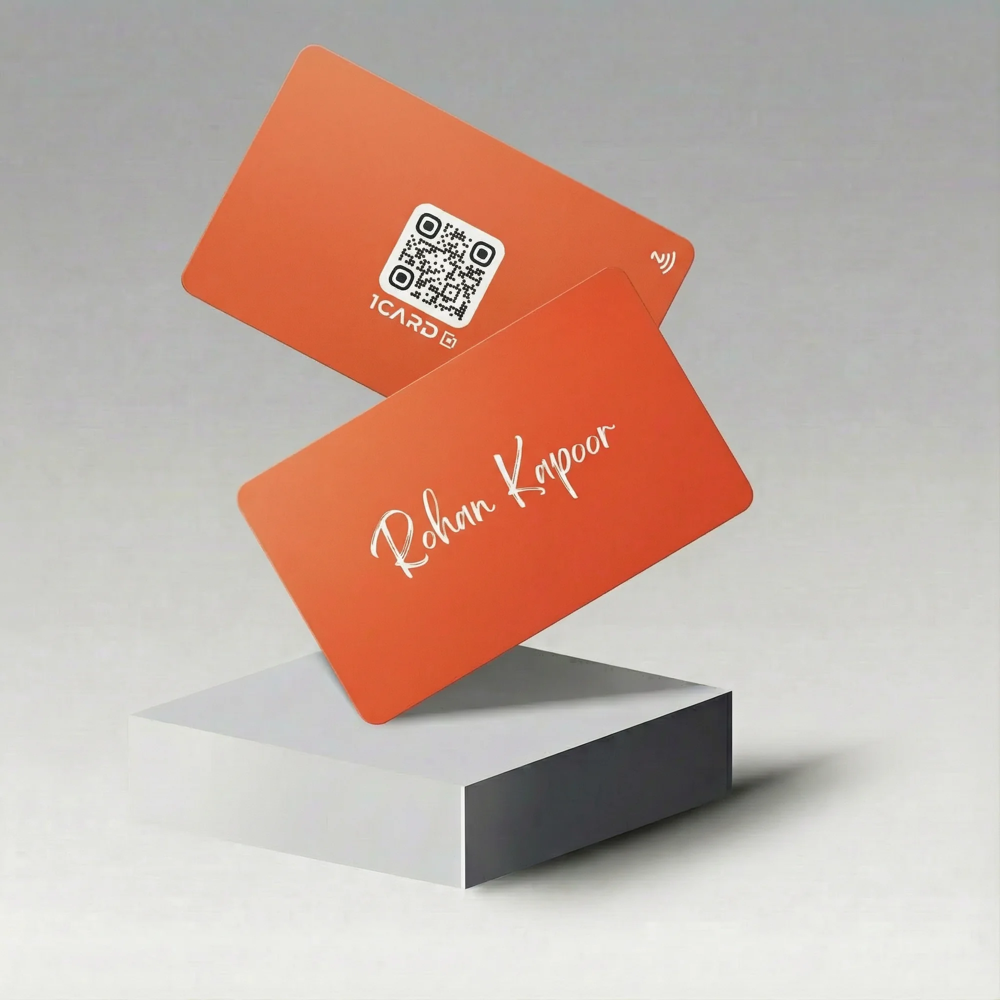 Two amber-colored NFC business cards with a QR code and name "Rohan Kapoor" displayed on a gray platform.