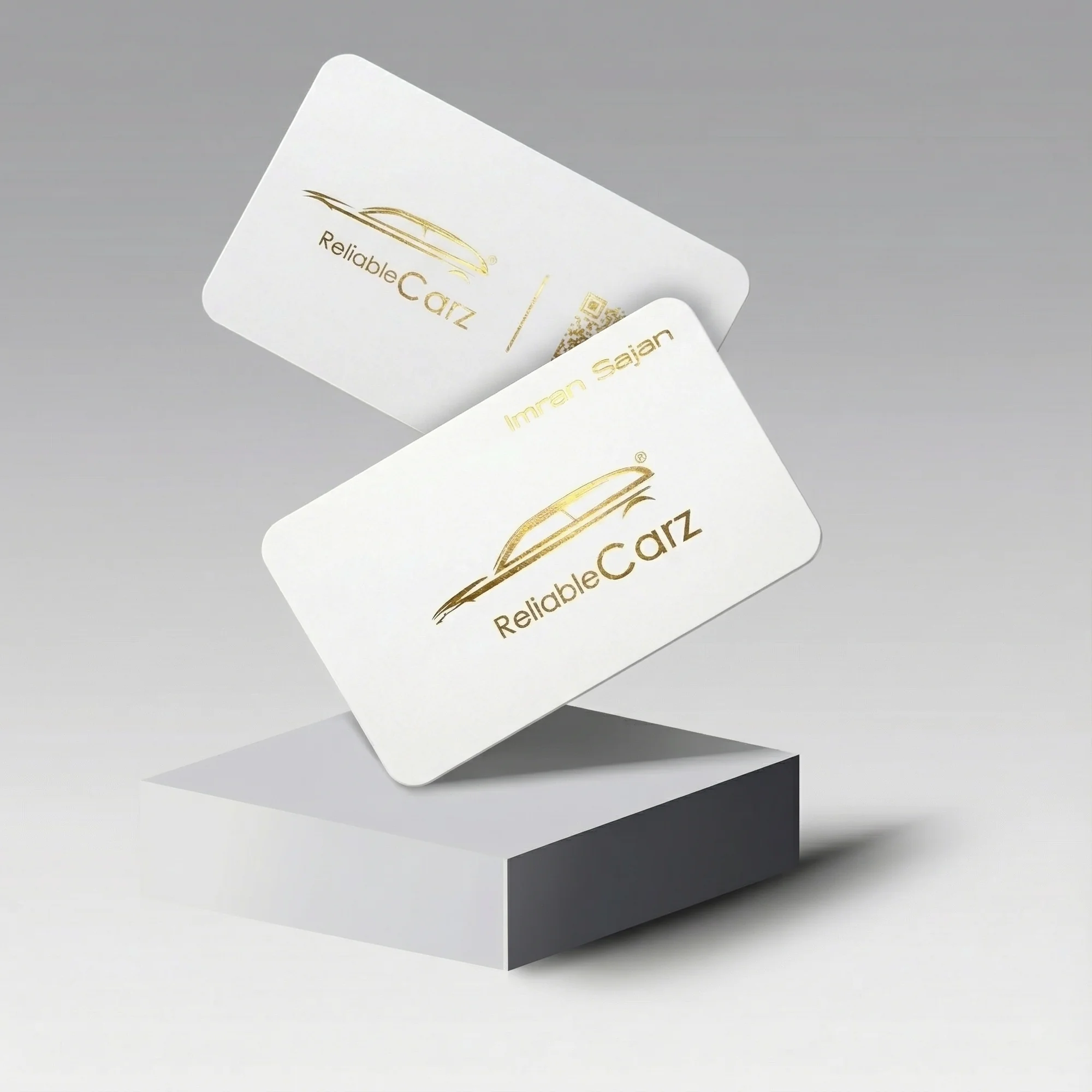 Two white cards with gold text and a car logo, displayed on a gray pedestal.