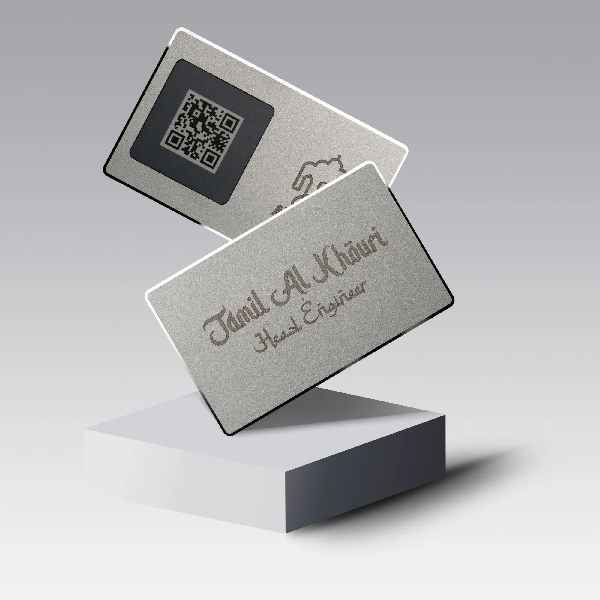 Two metallic cards with engraved text and a QR code, displayed on a white pedestal against a gradient background.