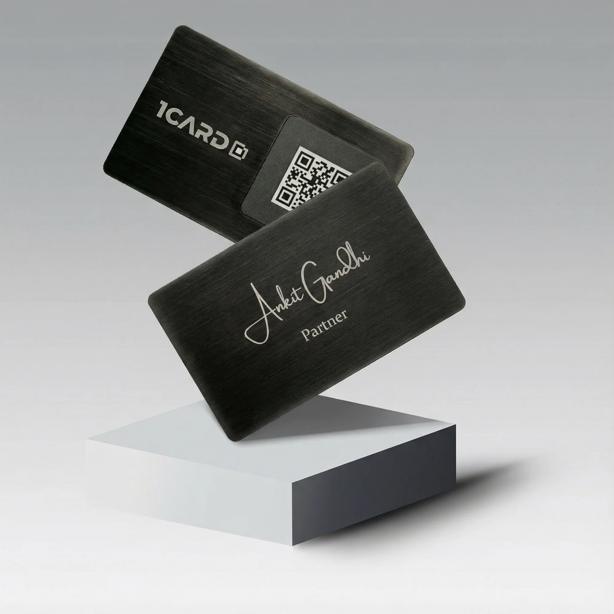 Two sleek black metal cards with engraved text and a QR code, displayed on a white platform.