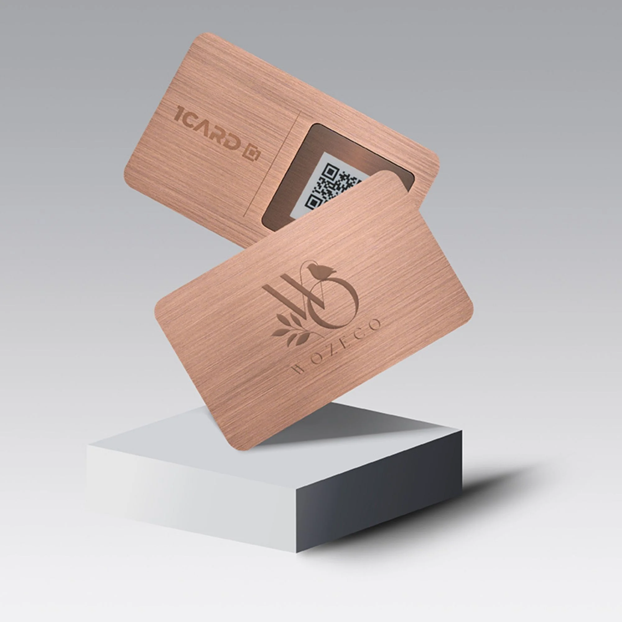 Two rose gold cards with engraved logos and a visible QR code, displayed on a geometric pedestal.