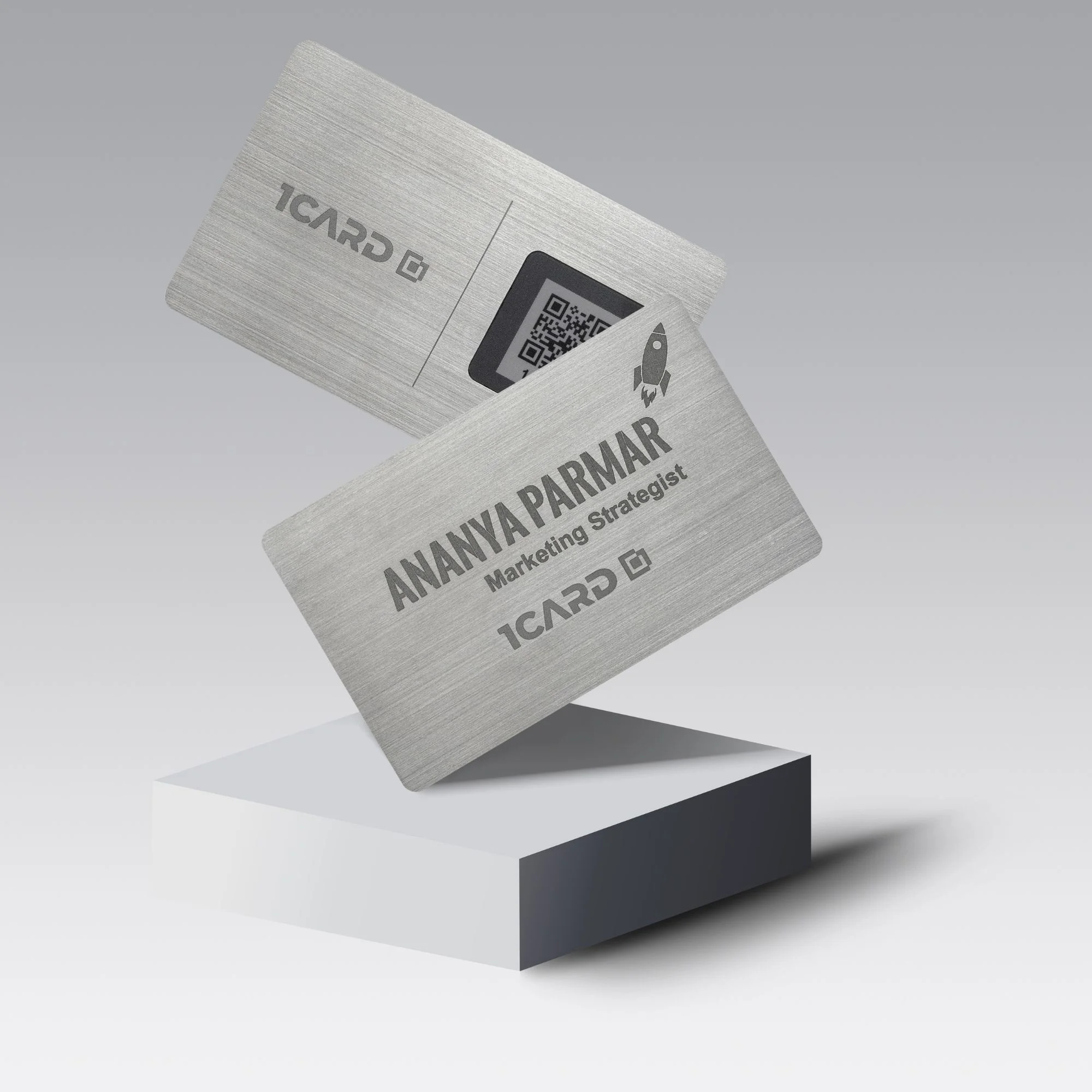 Two metallic cards with "1Card" logo and text, one showing a QR code, on a white pedestal.